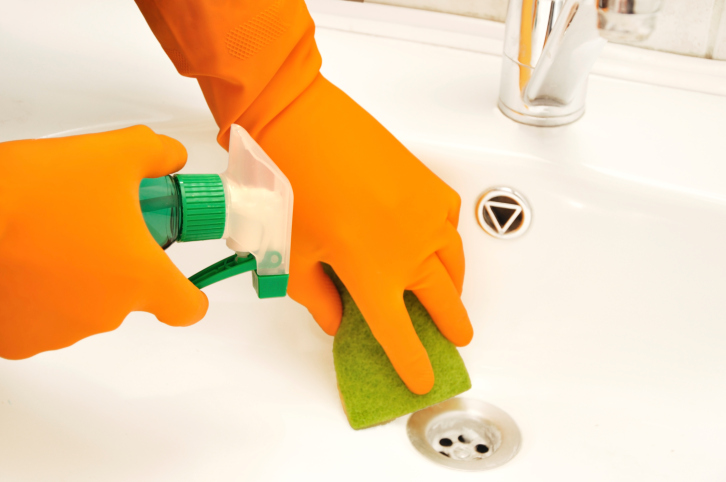 Cleaning a bathroom sink, using orange gloves