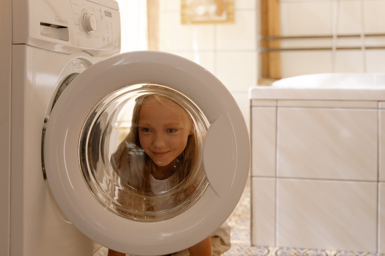 A girl looking through the front lid of a washing machine