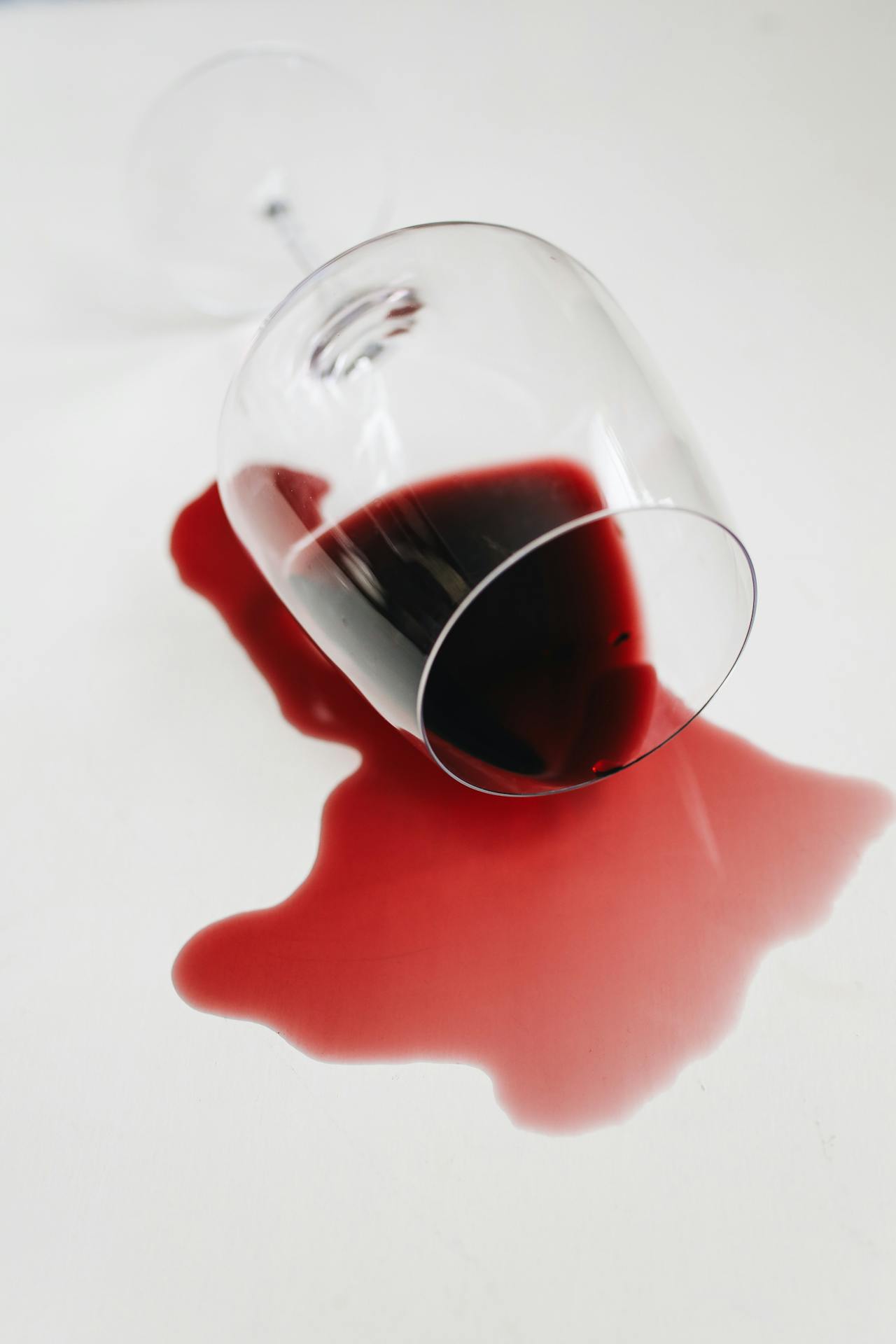 A glass of spilt red wine on a white surface